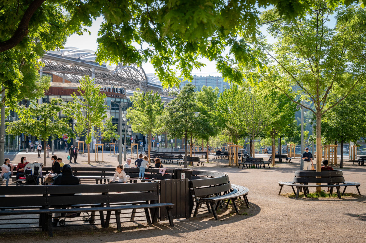 des familles profitent de l'ombre des arbres et des bancs sur l'esplanade Miterrand