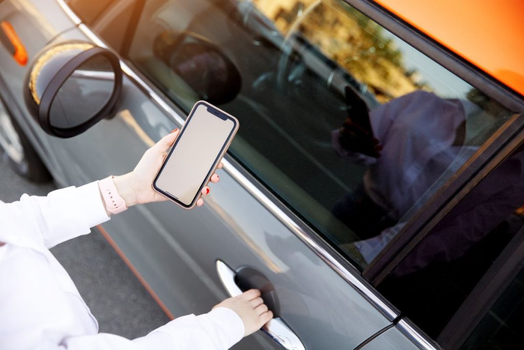 Gros plan sur les mains d'une femme qui utilise un portable et une application en ligne et se tient près d'une voiture pour ouvrir une poignée de portière. 