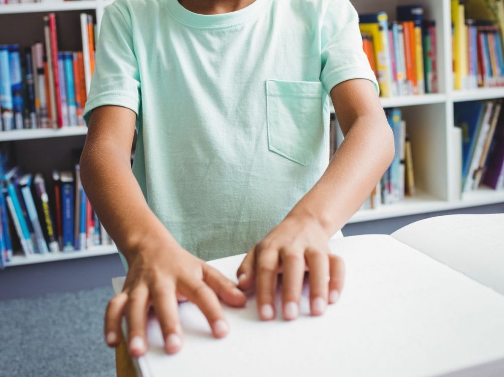 mains d'un jeune garçon qui utilisent le braille pour lire un livre